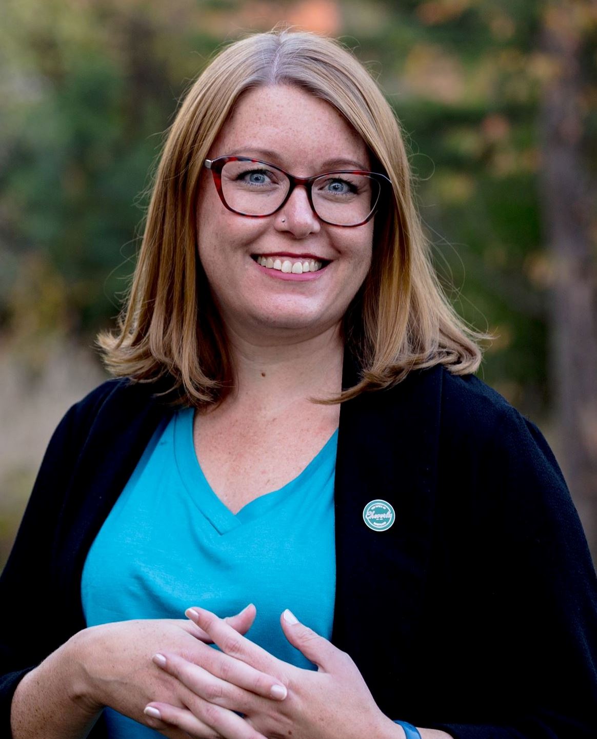 white woman with glasses, blue shirt and black jacket, standing outside